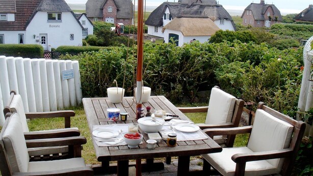 A picnic table set up outdoors with a thatched-roof house in the background. - House Wattblick App. WB/01 - Wattblick (Sylt)