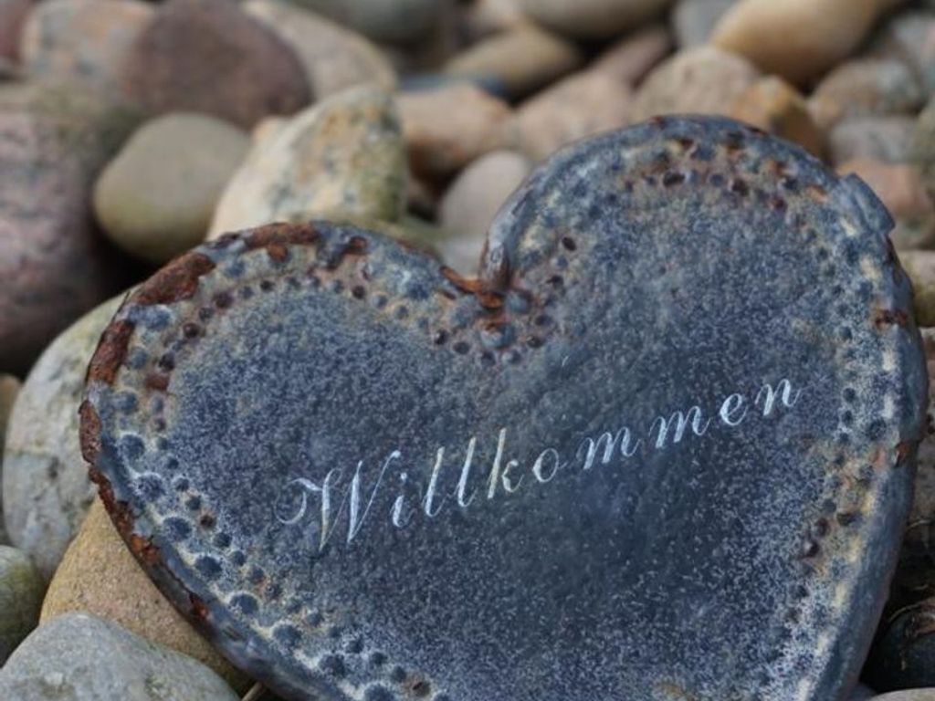 A heart-shaped stone with the inscription "Willkommen" on a bed of pebbles.