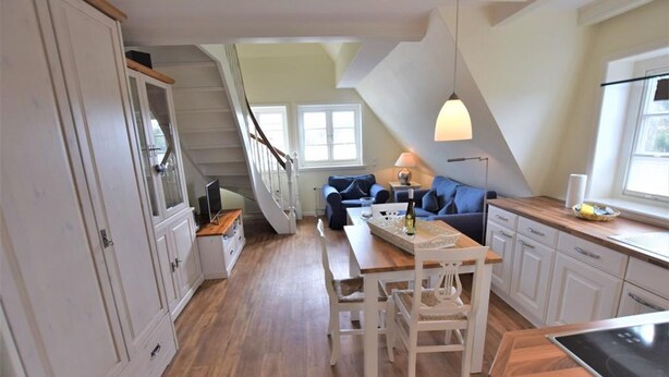 Eine geräumige Küche mit Holztisch und Stühlen, ein Essbereich mit einer Couch und eine Treppe, die zu einer oberen Ebene führt.