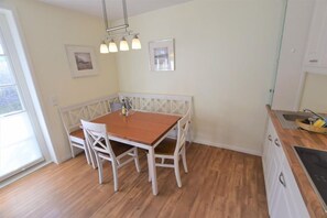 A small kitchen with a wooden table and white chairs, a bench, and a hanging light fixture. - Landhaus Ruusenhüs App. Ruu 05 - Landhaus Ruusenhüs (Sylt)