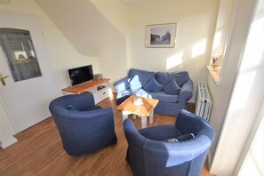 A compact living space with a sofa, two armchairs, a coffee table, a TV, and a radiator. - Landhaus Ruusenhüs App. Ruu 05 - Landhaus Ruusenhüs (Sylt)