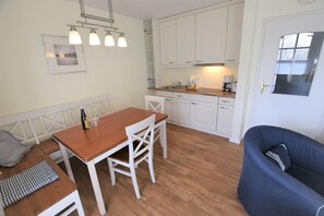 A compact kitchen with white cabinets, a wooden dining table, and a blue armchair.