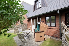 A patio with a table and chairs, a wicker chair, and a green chair. - Landhaus Ruusenhüs App. Ruu 05 - Landhaus Ruusenhüs (Sylt)