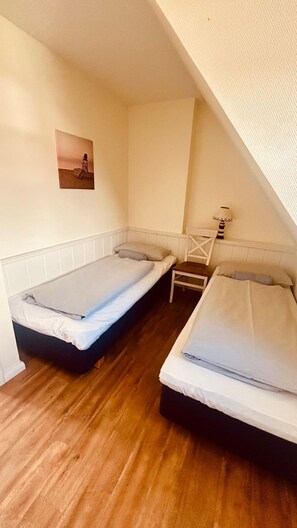 A small, enclosed room with two single beds, a chair, and a lamp. - Landhaus Ruusenhüs App. Ruu 05 - Landhaus Ruusenhüs (Sylt)