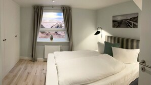 Un dormitorio con cama, mesita de noche, lámpara, ventana con cortinas y un cuadro en la pared.
