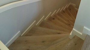 Una escalera con escalones de madera y paredes blancas, con apliques circulares que proporcionan luz.