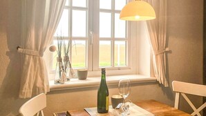 Un coin repas avec une table en bois, des chaises blanches, une bouteille et un verre à vin posés sur un tapis.