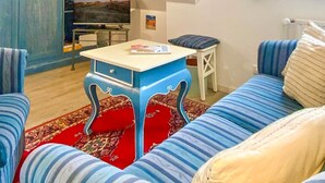 Un salon chaleureux avec un canapé bleu, un tapis à motifs rouges et un téléviseur en arrière-plan.