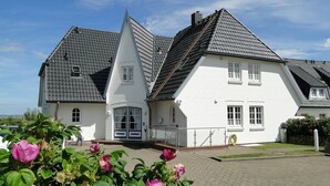 Une grande maison blanche à deux étages, dotée d’un toit à forte pente et d’une petite structure ressemblant à une tour.