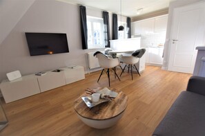 A modern living room with a flat-screen TV, a white entertainment unit, a wooden coffee table, and a grey sofa. - Warfthüs App. 08 - Warfthüs (Sylt)