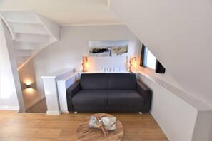 A modern living room with a dark grey sofa, a wooden coffee table, and a staircase on the left.