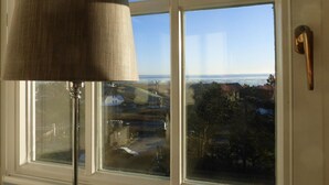 Una ventana con vista a un paisaje costero, una lámpara y un picaporte.