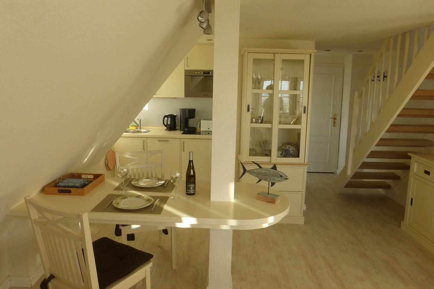 A compact kitchen with a dining area, a staircase, and a cabinet with glass doors.