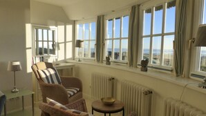 Una habitación con un ventanal amplio, muebles de mimbre, una mesita y un radiador.