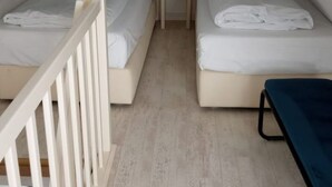 Una habitación con dos camas, una mesita y un banco azul.