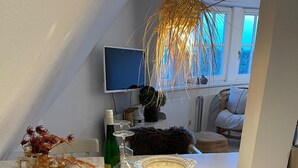 A dining area with a white table, two white chairs, a bottle of wine, a glass, and a decorative plate. - House Rundblick App. 06 - panoramic view (Sylt)