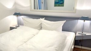 A neatly made bed with white bedding in a room with a wooden floor and a blue wall.