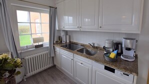 A kitchen with white cabinets, granite countertops, a built-in dishwasher, a coffee maker, and a window with curtains.