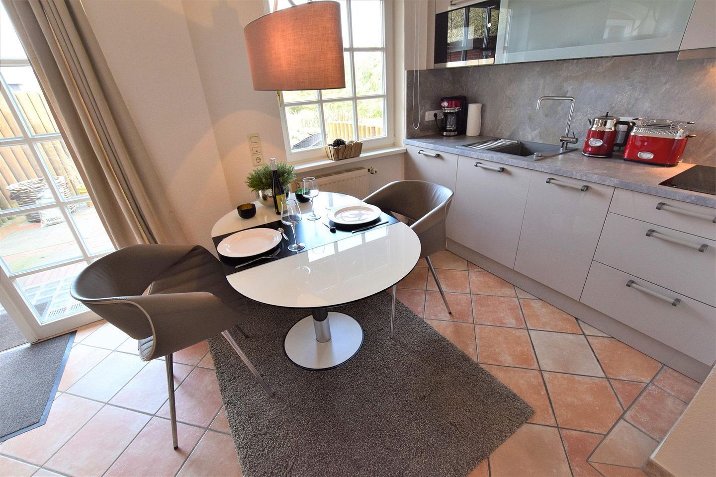 A modern kitchen with a dining area, featuring a round table, chairs, a coffee maker, and a toaster.