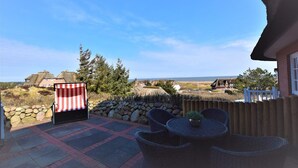 A patio with wicker furniture and a striped awning, overlooking a rural landscape with houses and a clear sky.