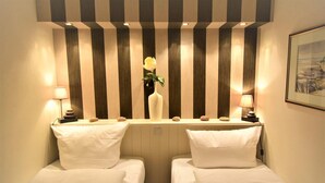 A hotel room with two single beds, a striped wall, a vase with a flower, and two bedside lamps.