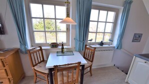 A dining area with a table and four chairs, a window with curtains, a radiator, and a small cabinet.