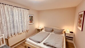 A bedroom with a bed, two bedside tables, a nightstand, a radiator, and curtains.