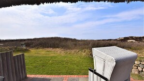 A patio with a wicker chair and a thatched roof overhead.
