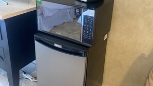 Un refrigerador compacto con un microondas y una cafetera encima, una etiqueta de garantía de 10 años y el logotipo de Samsung.