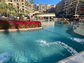 Une piscine à l’eau d’un bleu cristallin, entourée de fleurs rouges et de palmiers.