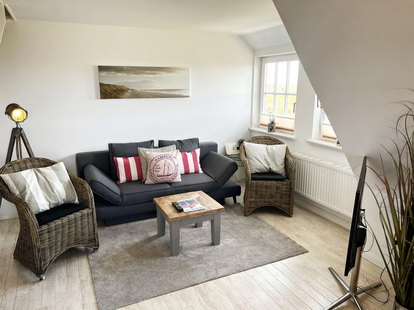 Ein Wohnzimmer mit einem dunklen Sofa, zwei Korbstühlen, einem Couchtisch und einem Gemälde an der Wand.