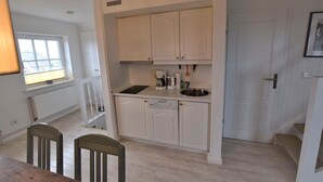 Cocina compacta con armarios blancos, lavavajillas integrado, cafetera y un lavamanos.