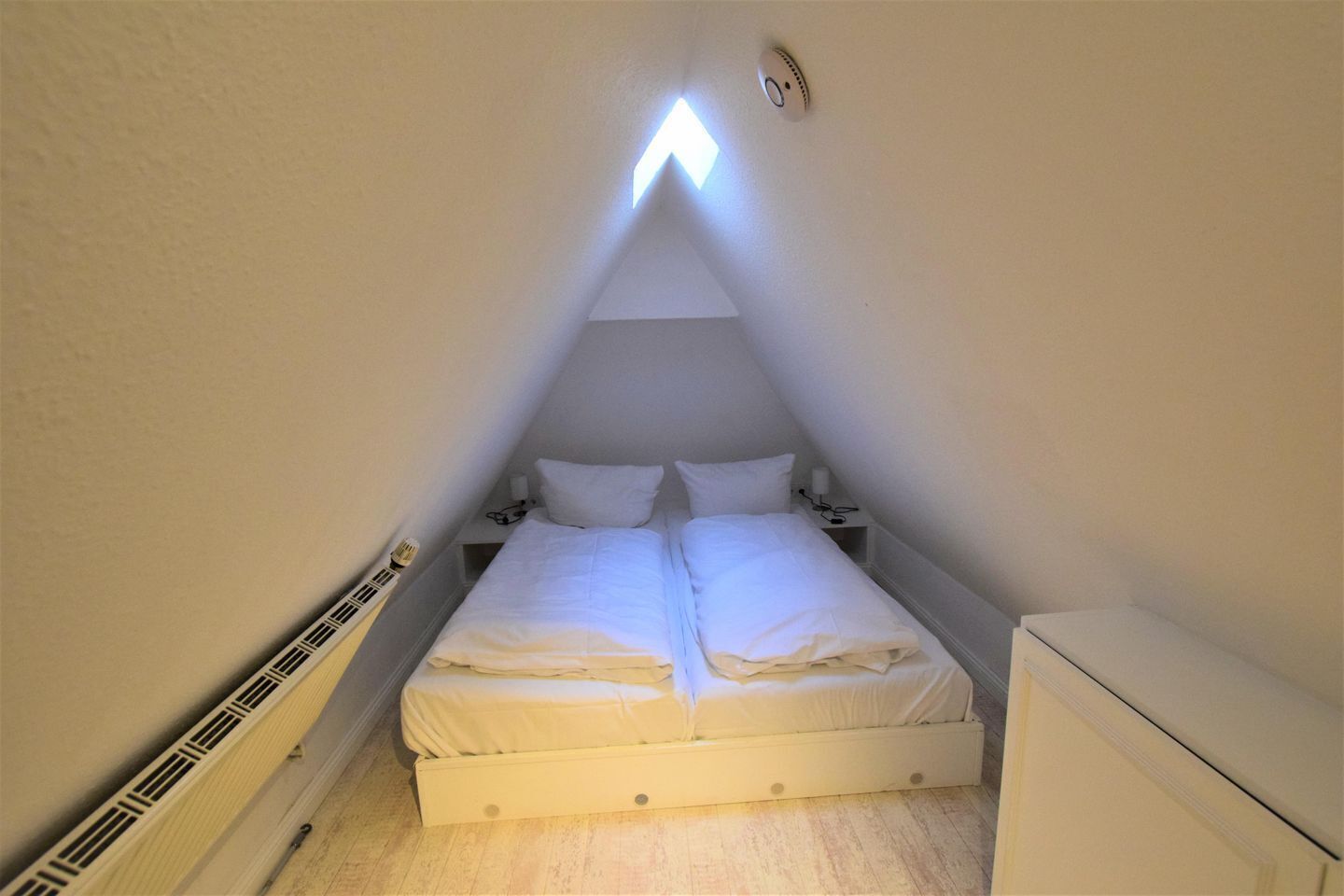 A small, narrow room with a single bed, a nightstand, and a desk.
