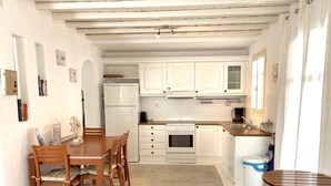 Een compacte keuken met witte kasten, een ingebouwde oven en een koelkast. Er is een eettafel met stoelen en een kleine ronde tafel.
