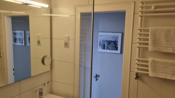 A bathroom with a mirror, a sink, a towel rack, and a door with a picture.