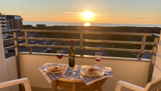 Un balcon avec une table dressée pour deux personnes, deux verres de vin rouge et une bouteille de vin.