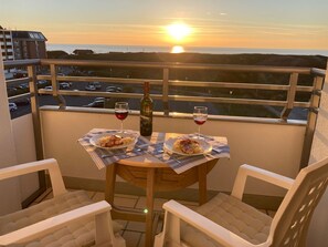 Un balcon avec une table dressée pour deux personnes, deux verres de vin rouge et une bouteille de vin.