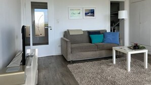 Un salon comprenant un canapé, une table basse, un téléviseur et une porte donnant sur une autre pièce.
