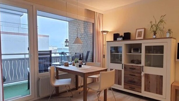 Un salon moderne avec une table à manger en bois, des chaises blanches, un meuble vitré et une vue sur un balcon.