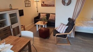 Un espace de vie compact comprenant une table à manger en bois, un canapé, un fauteuil à bascule, une petite table basse et un lit.