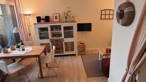 Un salon moderne avec une table à manger en bois, des chaises blanches, un téléviseur fixé au mur et un petit meuble avec des portes en verre.