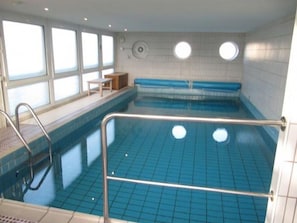 An indoor swimming pool with a blue tiled floor, a seating area with a bench, and a small table.