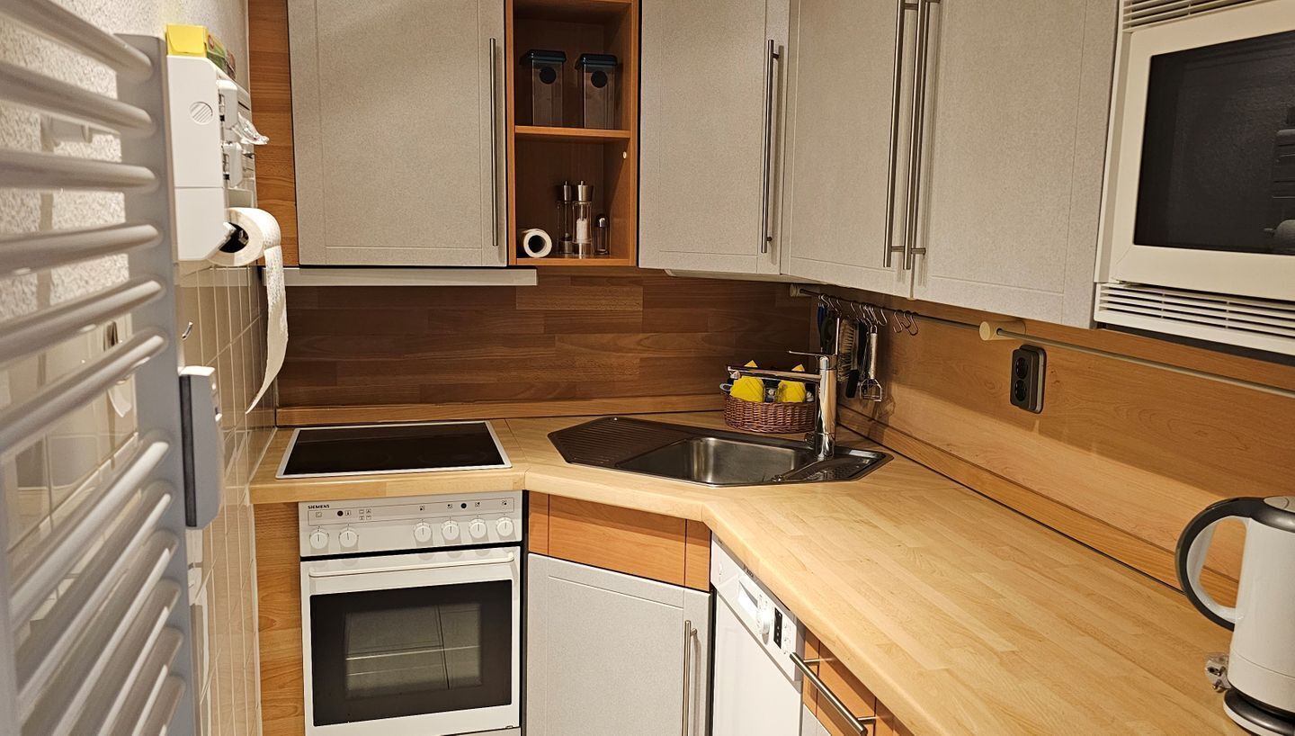 Een kleine keuken met een inbouwoven, een magnetron, een spoelbak en houten kastjes.