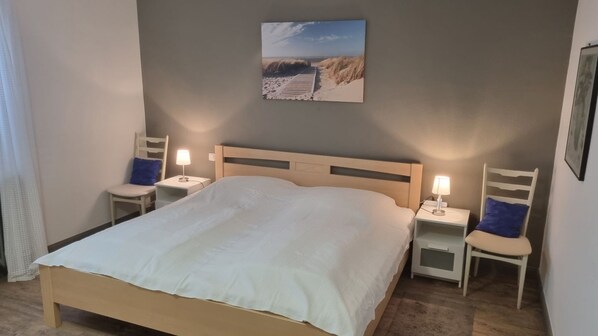 Une chambre à coucher avec un lit, deux tables de chevet, une lampe, une chaise et un tableau au mur.