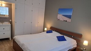 A bedroom with a large bed, two bedside tables with lamps, a wardrobe, a bathroom with a sink, and a painting of a beach on the wall. - house Bismarckstr. 40 apartments 40 - 3 room apartment with a beautiful terrace. (Sylt)