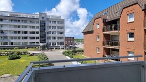 A modern apartment building with balconies, a courtyard, and a view of a street with cars and cyclists.