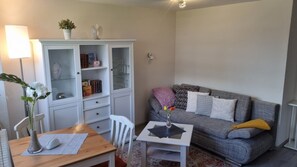 Un salon avec un canapé gris, un meuble blanc, une table à manger ornée d’un vase et une lampe.