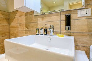 A modern bathroom with a large white bathtub, a mirror above it, and a wall-mounted water dispenser. - Appartamento Ulivo (Salò)