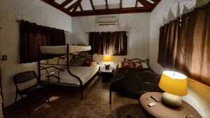A compact room with a bunk bed, a sofa, a small table with a lamp, and a chair.