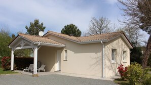 A two-story house with a covered patio, a satellite dish, and a gravel driveway. - Single-storey villa, large plot, close to lake and ocean (Hourtin)